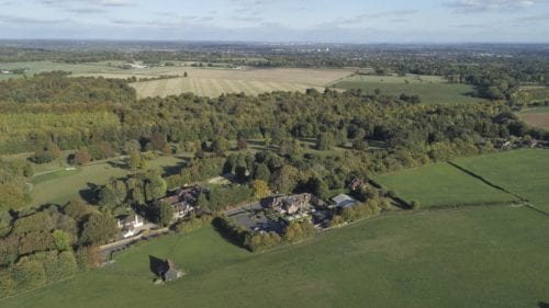 Hurley House - Aerial view of a rural landscape with clusters of houses surrounded by fields and forests. The horizon features distant patches of trees and open farmland under a sky with scattered clouds.