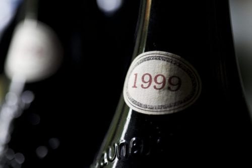 Hurley House - Close-up of a wine bottle with a label showing the year 1999, surrounded by dark glass and subtle reflections. The focus is on the vintage date, suggesting an aged or collectible wine.