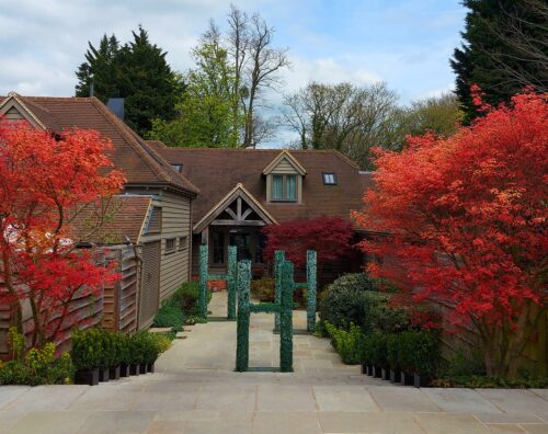 Hurley House - A house with steep gabled roofs is framed by vibrant red-orange trees and green shrubs along a paved pathway under a partly cloudy sky.