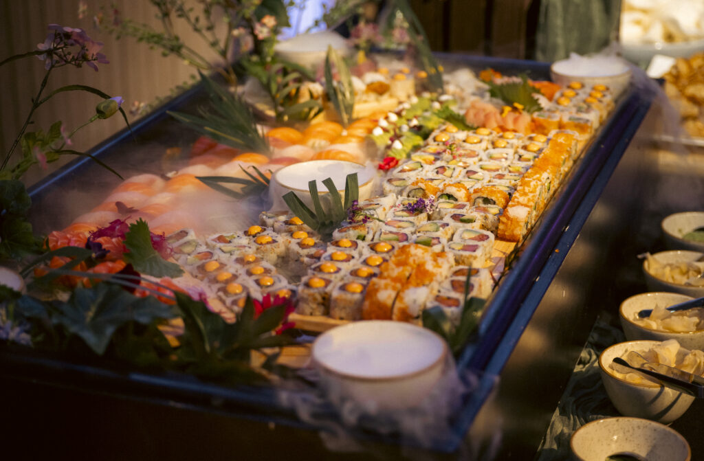Hurley House - A large platter of assorted sushi rolls and nigiri, garnished with green leaves and flowers, is displayed on a bed of ice at a buffet in a luxury wedding venue in Berkshire, with several small bowls of dipping sauces nearby.