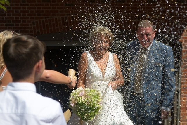 Hurley House - A bride holding a bouquet and a groom in a suit are showered with confetti at a luxury wedding venue in Berkshire. They smile as a young man in a white shirt and a woman with blonde hair join the celebration outside the charming brick building.