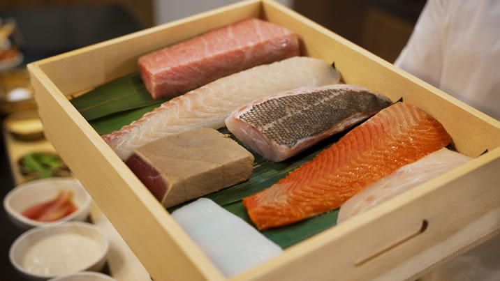 Hurley House - A wooden tray displays various fresh fish fillets and cuts, including salmon, tuna, and white fish, arranged neatly on green leaves.