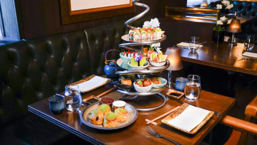Hurley House - A stylish restaurant table set for two, featuring an elaborate metal stand with tiers of assorted sushi, small dishes, and desserts, along with teapots, cups, and plates arranged neatly on a dark wooden table.